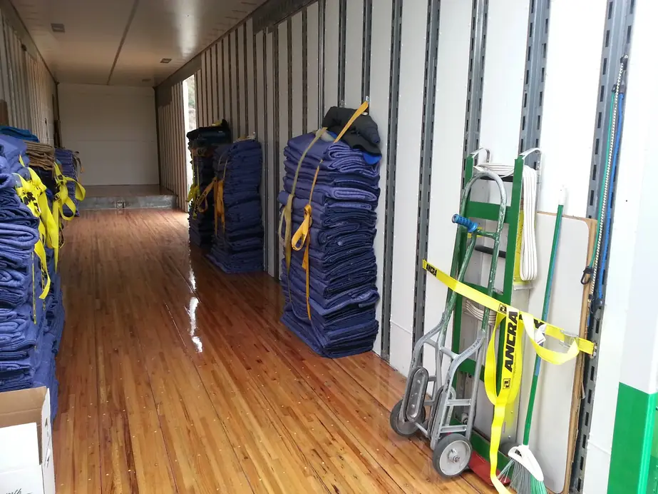 Inside a Farnsworth van: wood floor, stacked blue moving pads, ratchet straps and hand trucks ready to load